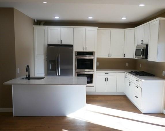 kitchen with appliances with stainless steel finishes, white cabinets, a sink, and wood finished floors