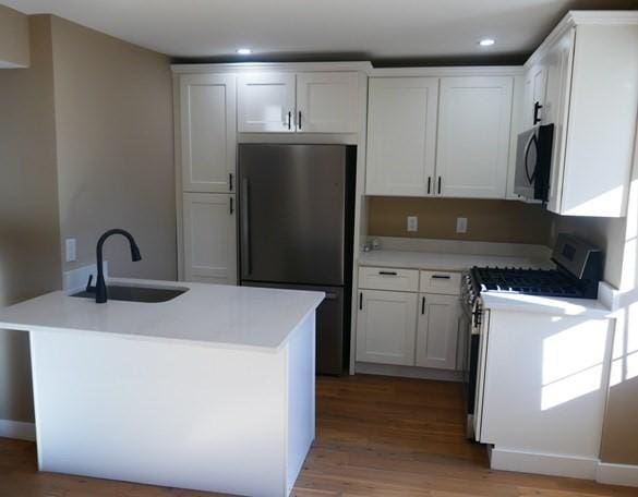 kitchen featuring stainless steel appliances, light countertops, white cabinetry, a sink, and light wood-type flooring