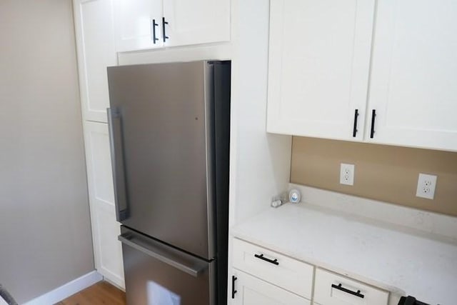 kitchen with light wood finished floors, baseboards, white cabinets, freestanding refrigerator, and light countertops