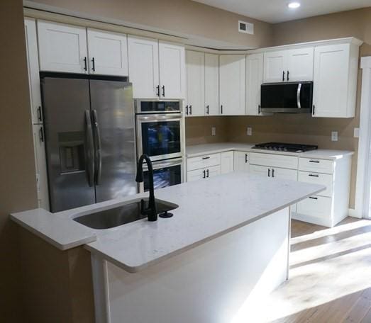 kitchen with stainless steel appliances, visible vents, white cabinetry, a sink, and light stone countertops