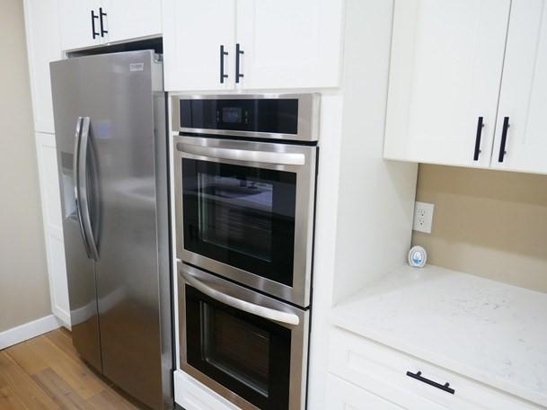 kitchen featuring appliances with stainless steel finishes, white cabinets, light wood-style flooring, and light stone countertops