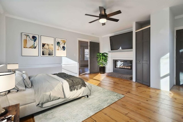 bedroom featuring hardwood / wood-style floors, ceiling fan, a fireplace, and crown molding