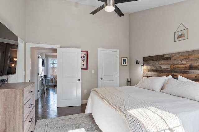 bedroom featuring dark wood-type flooring, a towering ceiling, baseboards, and a ceiling fan