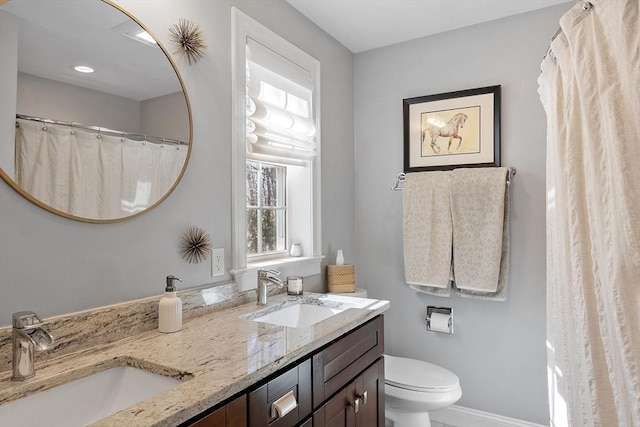 bathroom featuring toilet, double vanity, baseboards, and a sink