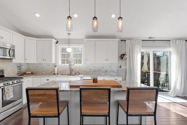 kitchen featuring white cabinets, dark wood-style floors, stainless steel appliances, a kitchen bar, and a sink