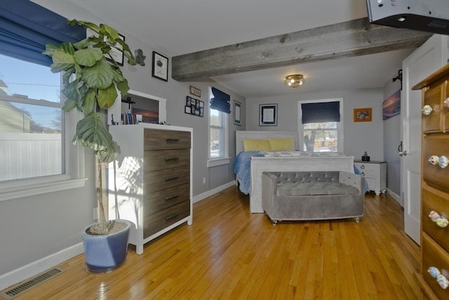 bedroom featuring light wood-style floors, baseboards, visible vents, and beam ceiling