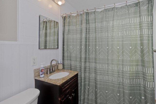 full bathroom featuring toilet, a shower with curtain, a decorative wall, and vanity