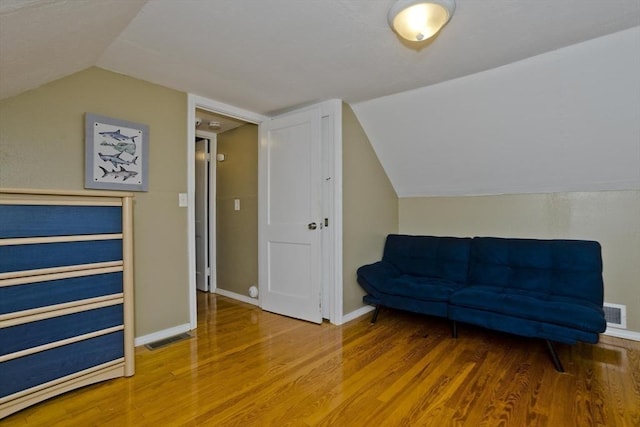 sitting room with lofted ceiling, wood finished floors, visible vents, and baseboards