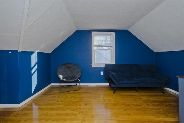 living area featuring lofted ceiling, a textured ceiling, baseboards, and wood finished floors