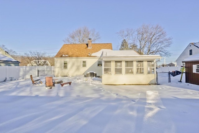 snow covered rear of property with a chimney, fence, and a fire pit