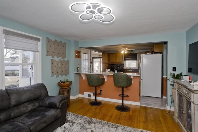 kitchen with a peninsula, light wood-style floors, light countertops, freestanding refrigerator, and a kitchen bar