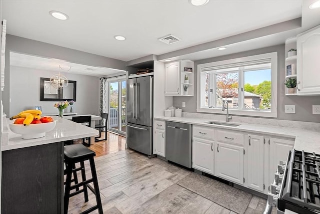 kitchen with open shelves, appliances with stainless steel finishes, a sink, white cabinetry, and a kitchen bar