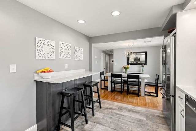 kitchen with appliances with stainless steel finishes, light countertops, a chandelier, a breakfast bar, and recessed lighting