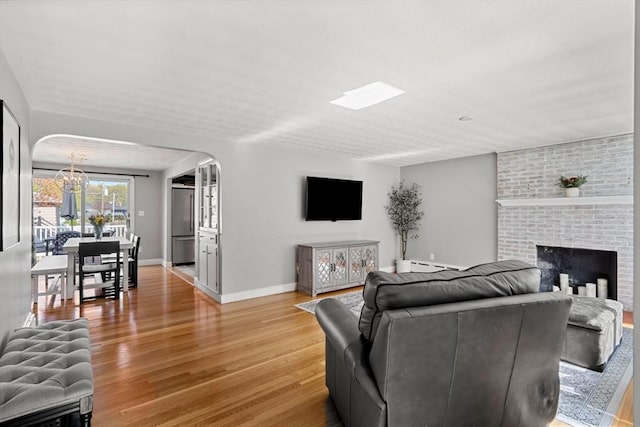 living room featuring a brick fireplace, light wood-style floors, a baseboard heating unit, a chandelier, and arched walkways
