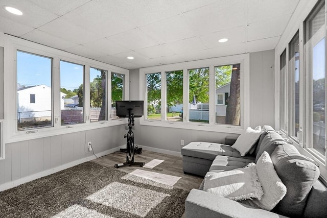 sunroom / solarium featuring baseboards, plenty of natural light, wood finished floors, and a paneled ceiling