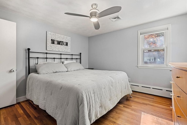 bedroom with ceiling fan, a baseboard radiator, wood finished floors, and visible vents