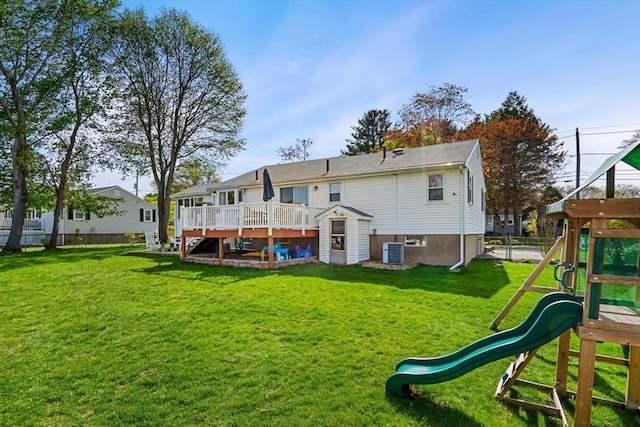 back of property with a playground, a wooden deck, a yard, and central AC