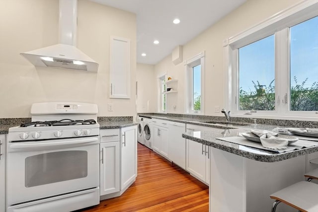 kitchen with white appliances, island exhaust hood, a sink, washer / clothes dryer, and white cabinets