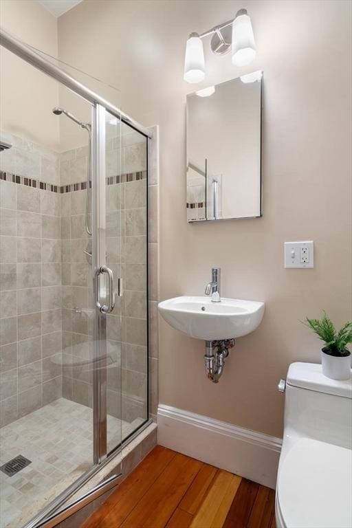 bathroom with baseboards, a shower stall, toilet, wood finished floors, and a sink