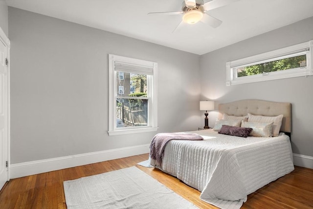 bedroom featuring multiple windows, baseboards, wood finished floors, and ceiling fan