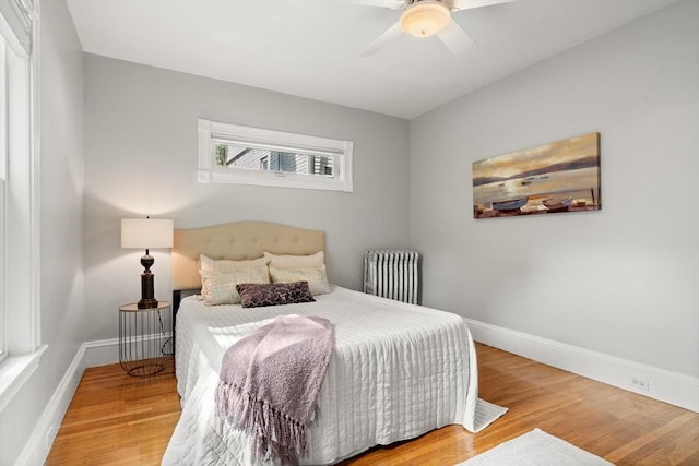 bedroom featuring radiator, baseboards, wood finished floors, and ceiling fan