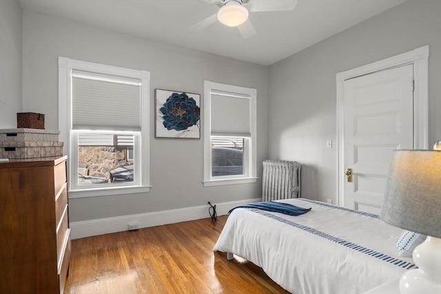 bedroom with radiator, baseboards, light wood-style flooring, and ceiling fan
