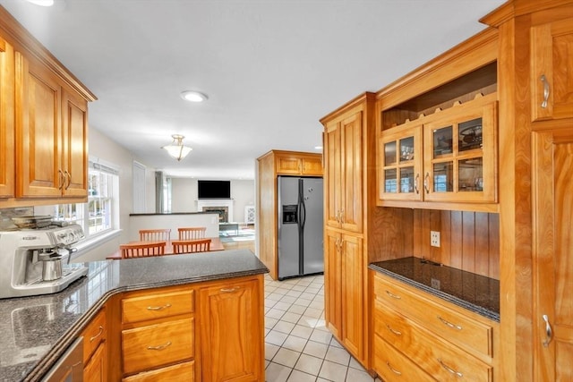 kitchen with stainless steel refrigerator with ice dispenser, light tile patterned flooring, and dark stone countertops