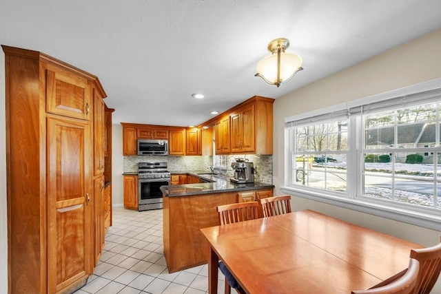 kitchen with decorative backsplash, light tile patterned floors, appliances with stainless steel finishes, and kitchen peninsula