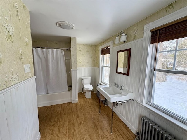 full bathroom with a wainscoted wall, toilet, radiator heating unit, and wallpapered walls