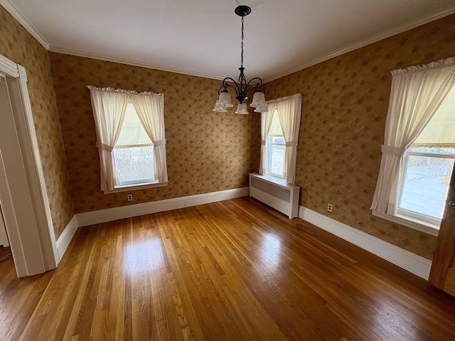 unfurnished dining area featuring wood finished floors, baseboards, radiator heating unit, and wallpapered walls