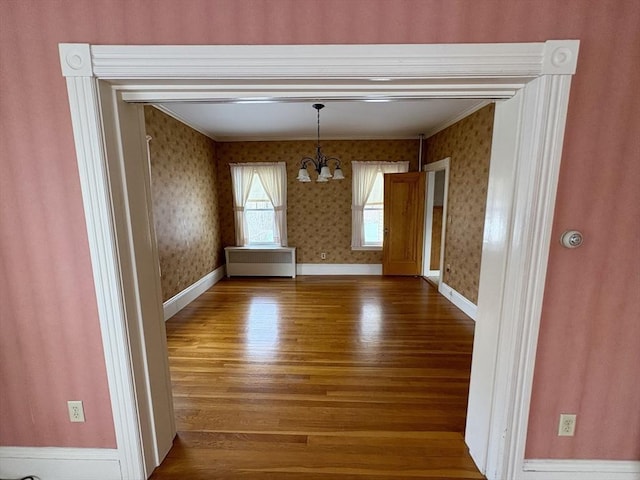 unfurnished dining area with wood finished floors, a notable chandelier, baseboards, and wallpapered walls