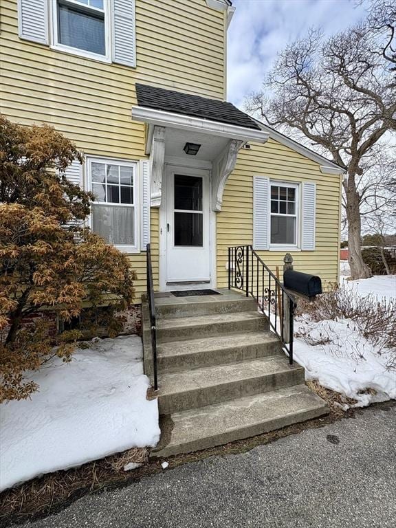 snow covered property entrance featuring roof with shingles