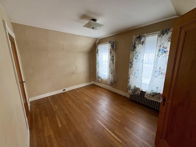 spare room with vaulted ceiling, radiator heating unit, wood finished floors, and baseboards