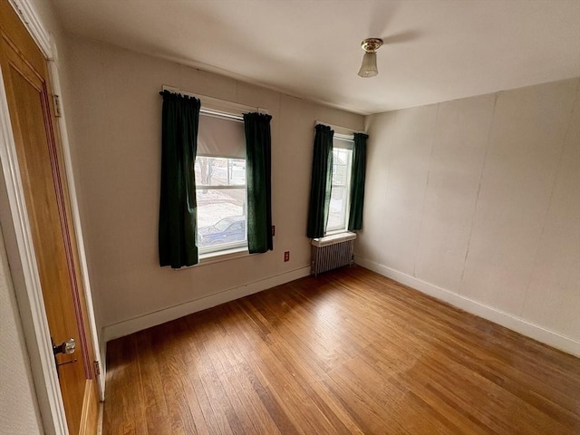 empty room with radiator heating unit, light wood-type flooring, and baseboards