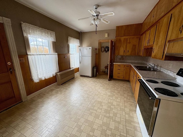 kitchen with radiator, electric range oven, brown cabinetry, freestanding refrigerator, and a sink