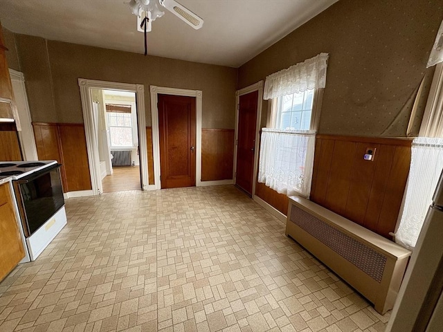 interior space with radiator, a wainscoted wall, electric range, and a ceiling fan