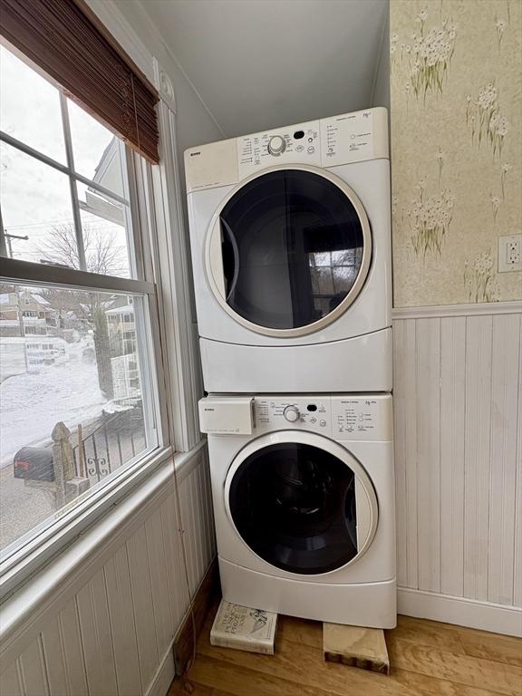 washroom featuring light wood-style floors, laundry area, a wainscoted wall, and stacked washing maching and dryer