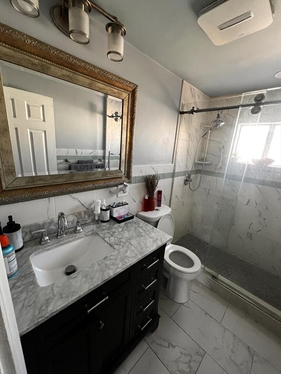 bathroom with walk in shower, vanity, toilet, and tile walls