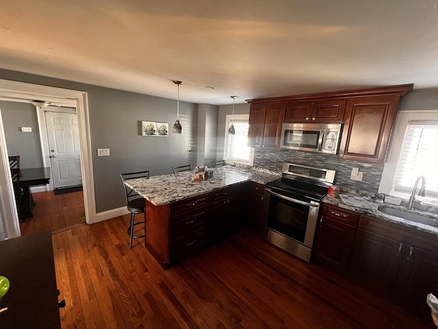 kitchen featuring sink, a breakfast bar area, stainless steel appliances, decorative light fixtures, and kitchen peninsula