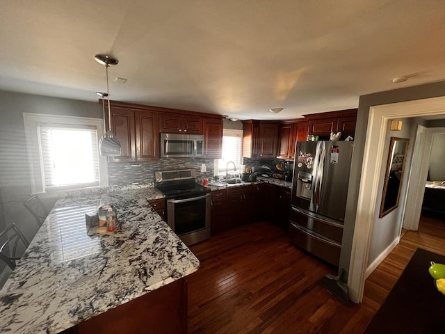 kitchen featuring light stone counters, hanging light fixtures, appliances with stainless steel finishes, dark hardwood / wood-style flooring, and backsplash