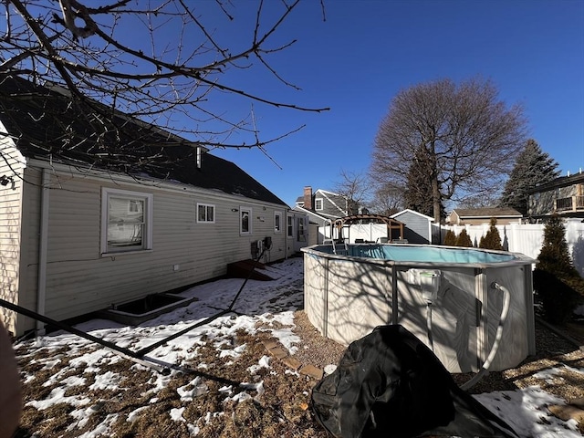 view of snow covered exterior with a fenced in pool and a storage unit