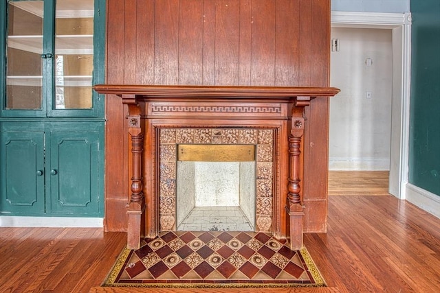 room details featuring a tiled fireplace, wood finished floors, and baseboards