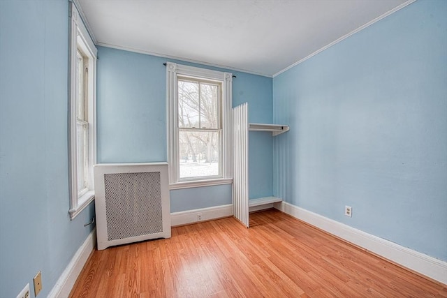 spare room with baseboards, crown molding, radiator heating unit, and wood finished floors