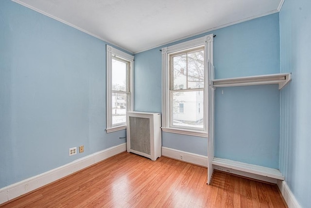 empty room with radiator heating unit, crown molding, baseboards, and wood finished floors