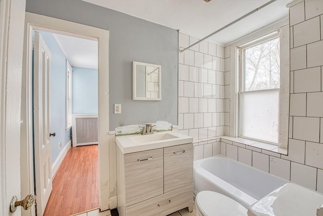 full bath featuring toilet, a bathing tub, vanity, wood finished floors, and baseboards