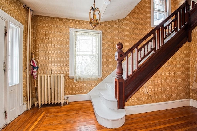 stairway with radiator, wallpapered walls, wood-type flooring, and baseboards