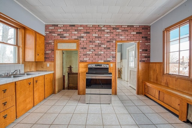 kitchen with light tile patterned floors, tile counters, wainscoting, stainless steel electric range, and a sink