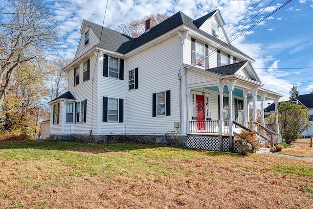 view of front facade featuring roof with shingles, a chimney, a porch, and a front yard