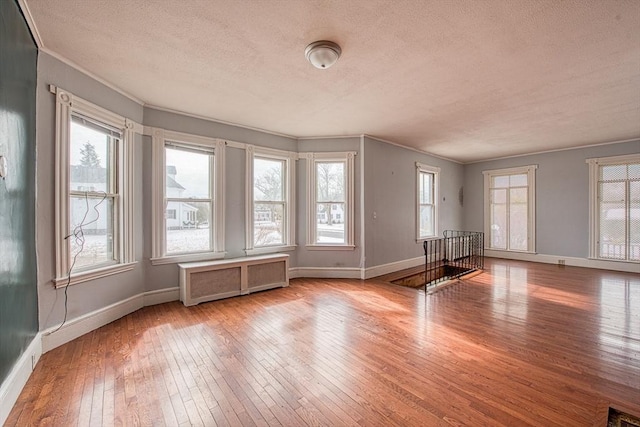 unfurnished room with baseboards, wood-type flooring, a wealth of natural light, and radiator