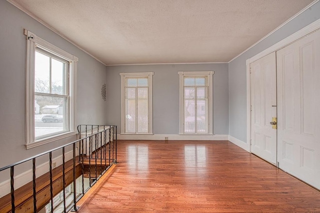 interior space featuring light wood finished floors, baseboards, a textured ceiling, and ornamental molding